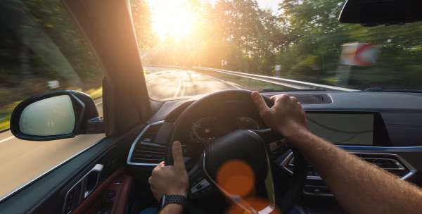 Ego-Perspektive einer Fahrt in einem Auto mit einer Straße, Bäumen und Sonne im Hintergrund